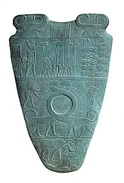 Reverso de la Paleta de Narmer, hacia el 3100 aC. La fila superior representa a cuatro hombres que llevan estándares. Sobre ellos es un Serej que contiene el nombre del rey, Narmer